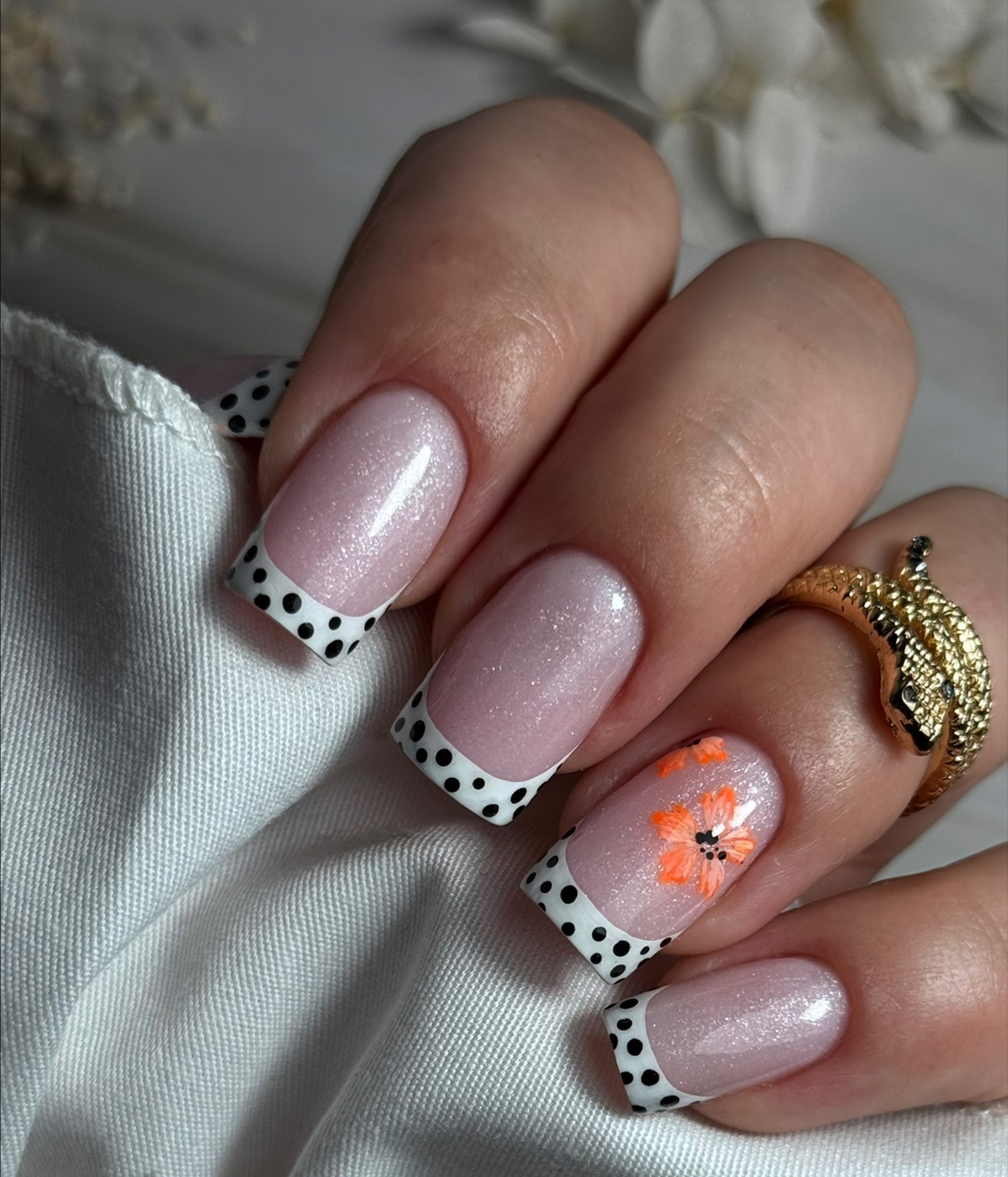 Glinsterend roze met witte French tips met zwarte stippen en een oranje bloem