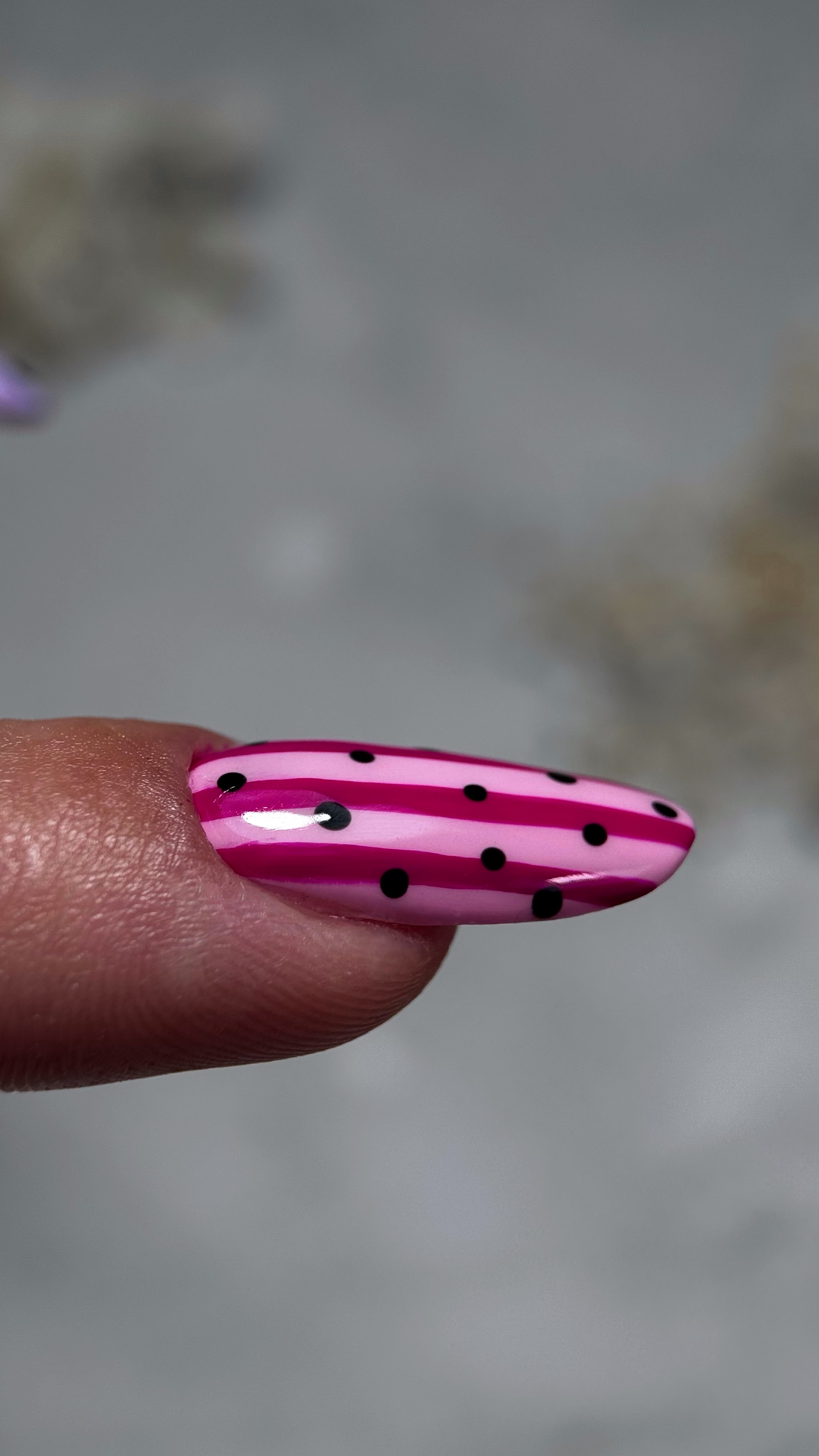 Close-up van een lange nagel met roze strepen en zwarte stippen